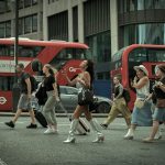 Crowd crossing a London street with iconic red buses in motion, capturing urban life.